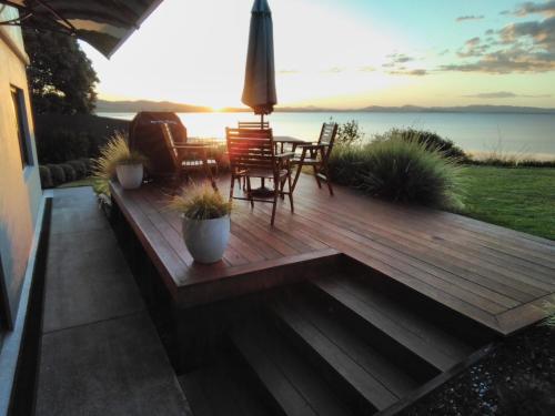 una terraza de madera con mesa, sillas y el océano en Harbourside Getaway, en One Tree Point