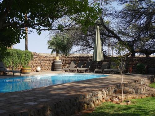 a swimming pool with a stone wall and a umbrella at Kalahari Farmhouse Campsite in Stampriet