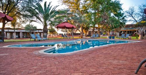 a swimming pool with chairs and umbrellas in a park at Kalahari Anib Campsite in Hardap