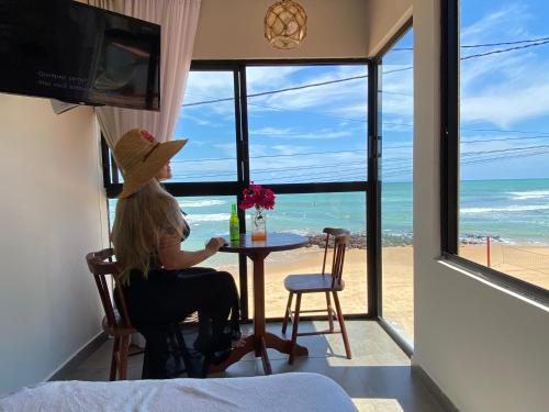 una mujer sentada en una mesa mirando hacia el océano en SuRFCoRe House en Baía Formosa