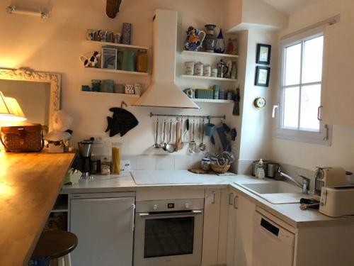 une cuisine avec des armoires blanches, un évier et une fenêtre dans l'établissement La Maison Bleue, authentique et charmante maison de pêcheur, à Trouville-sur-Mer