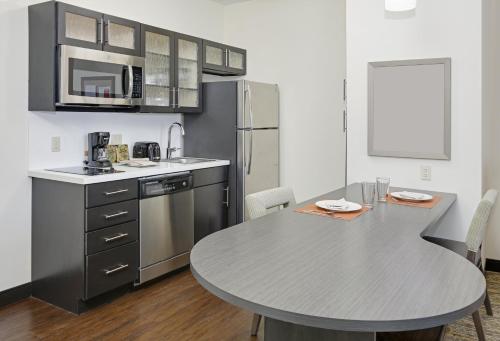 a kitchen with a table and a stainless steel refrigerator at Candlewood Suites Dallas NW - Farmers Branch by IHG in Farmers Branch