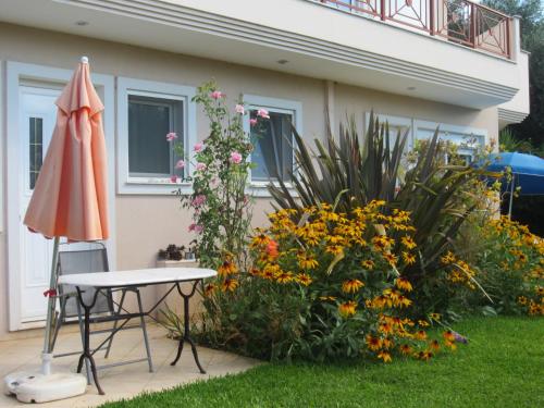 a patio with a table and an umbrella and flowers at Villa Verde Apart-Hotel in Nea Makri