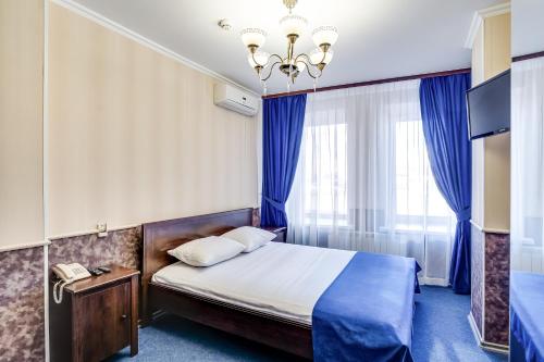 a bedroom with a bed with blue curtains and a chandelier at Hotel Teatralny in Rostov on Don