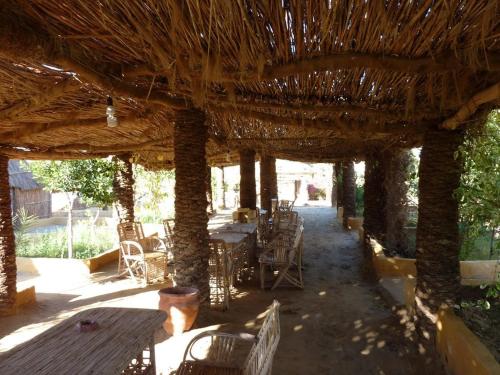 a patio with tables and chairs under a straw roof at Badry Sahara Camp in Bawiti