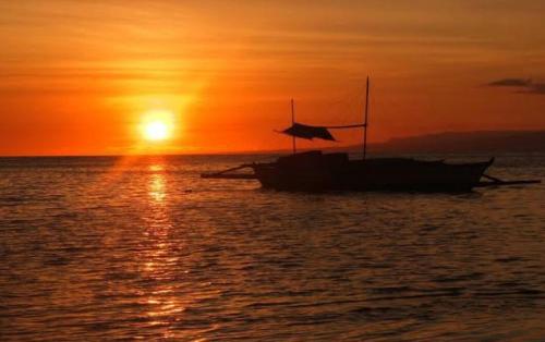 a boat sitting in the ocean at sunset at First Baby Bytes Guest House in Siquijor