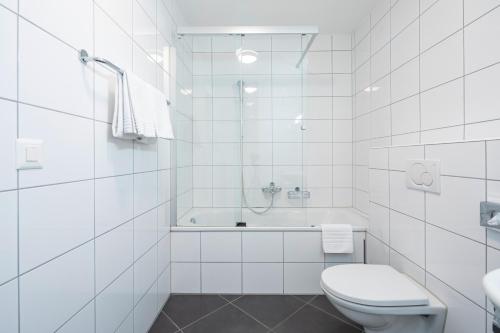 a white bathroom with a toilet and a bath tub at Marina Walensee Hotel in Unterterzen