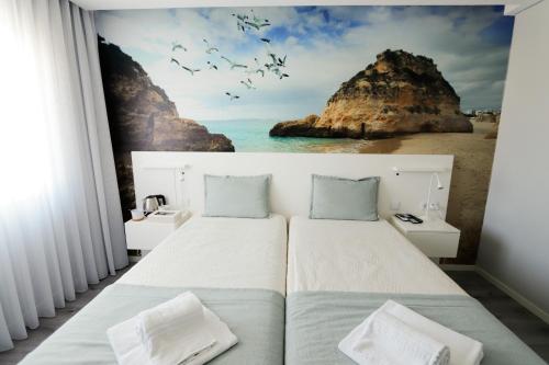 a bedroom with two beds and a painting of the ocean at Golden Beach Guest House & Rooftop Bar in Faro