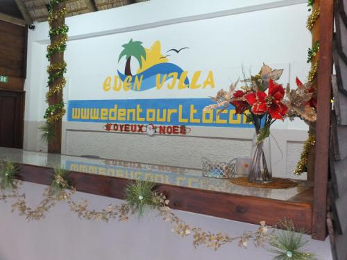 a sign for a resort with a vase of flowers on a counter at Eden Villa in Belle Mare