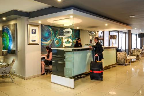 a man with a suitcase standing at a counter in a restaurant at The Nicol Hotel and Apartments in Johannesburg