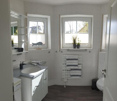 a white bathroom with a sink and two windows at Haus Seeteufel in Zingst