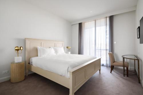 - une chambre avec un grand lit blanc et une chaise dans l'établissement Knightsbridge Canberra, à Canberra