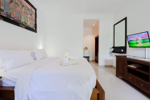 a bedroom with a white bed and a flat screen tv at WIRA Homestay & Spa in Uluwatu