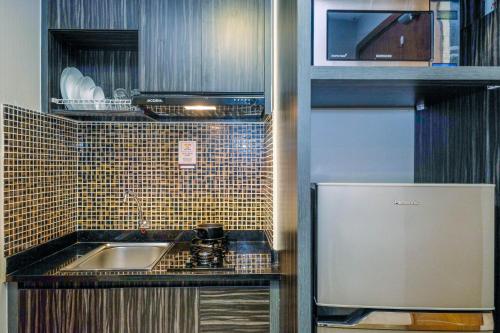 a small kitchen with a sink and a refrigerator at Warm and Cozy Studio at The Oasis Cikarang Apartment By Travelio in Cikarang