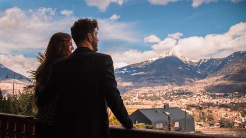 a man and woman sitting on a bench looking at the mountains at Hotel Traubenwirt in Marlengo