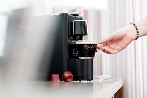a person holding a cup of coffee next to a coffee machine at Fora Hotel Hannover by Mercure in Hannover