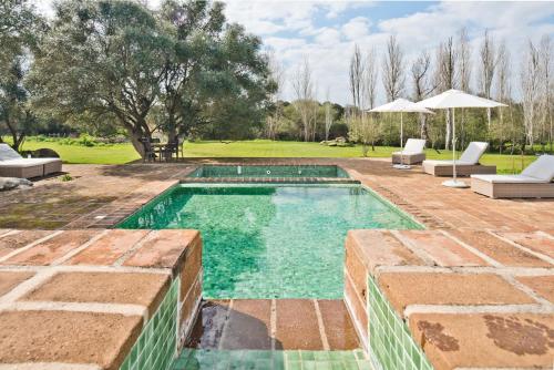 a swimming pool in a yard with chairs and an umbrella at Herdade do Barrocal de Baixo in Montemor-o-Novo