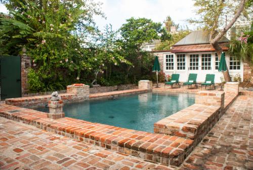 a pool with a brick retaining wall and chairs in a yard at Audubon Cottages in New Orleans