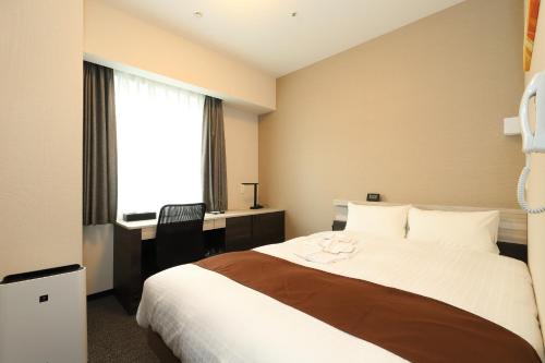 a bedroom with a bed and a desk and a window at Smile Hotel Premium Osaka Higashishinsaibashi in Osaka