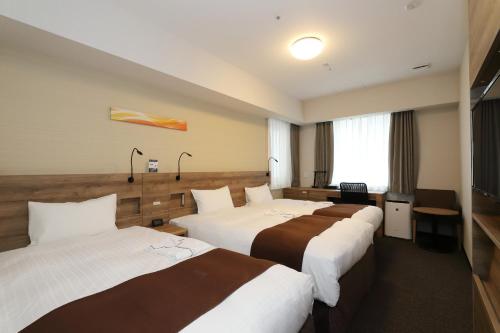 a hotel room with three beds and a television at Smile Hotel Premium Osaka Higashishinsaibashi in Osaka