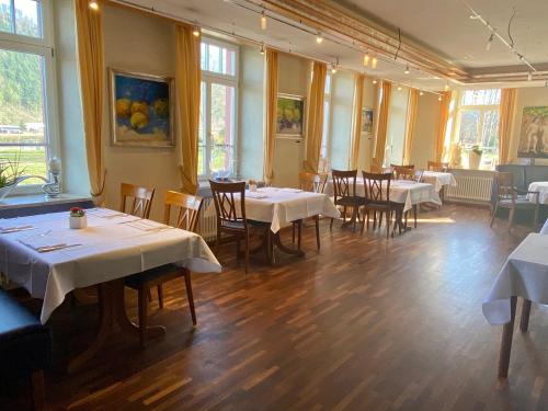 une salle à manger avec des tables blanches, des chaises et des fenêtres dans l'établissement Landhaus Hechtsberg, à Hausach