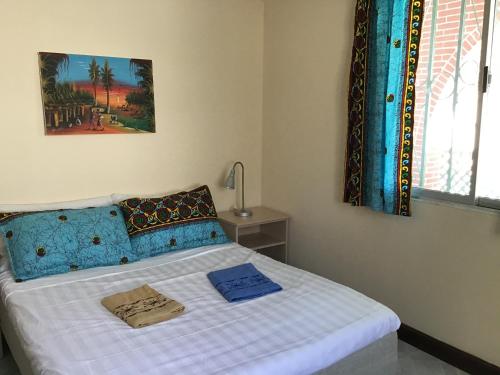 ein Schlafzimmer mit einem Bett mit blauen Kissen und einem Fenster in der Unterkunft Anns Guesthouse BakauGambia in Bakau