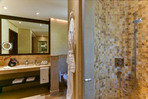 a bathroom with a shower and a sink and a mirror at Kempinski Hotel Ishtar Dead Sea in Sowayma