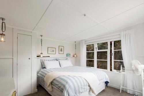 a white bedroom with a bed and a window at Kiwiana Bach - Lake Tarawera Holiday Home in Lake Tarawera