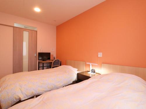 two beds in a room with orange walls at Hotel Asahi Grandeur Fuchu in Fuchu