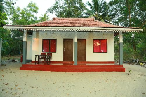 een klein huis met een rood dak op het strand bij Marari Baiju's Homestay in Mararikulam