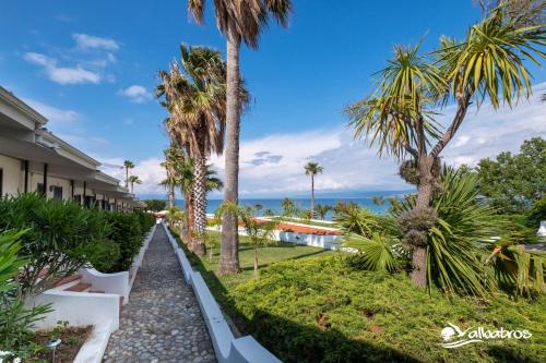 a walkway through a resort with palm trees and the ocean at Residence Albatros in Briatico