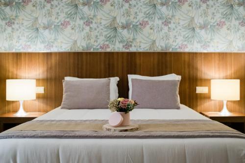 Una cama con dos lámparas y un jarrón con flores. en Quinta do Pinheiro Hotel Rural - GQL, en Valado dos Frades