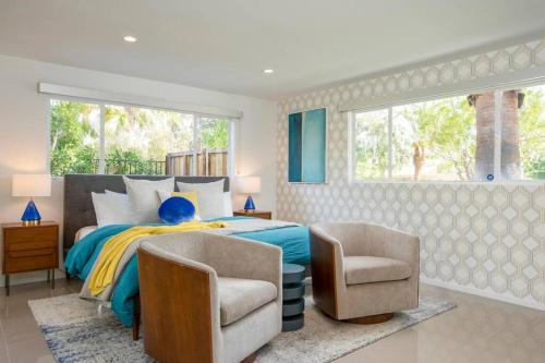 a bedroom with a bed and two chairs and a window at Villa Perfetto Plaza in Palm Springs