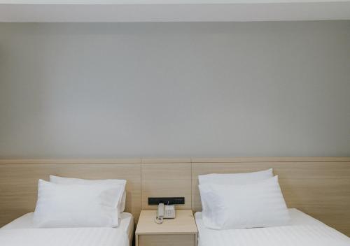 two beds with white pillows and a phone between them at The Rich Hotel in Nakhon Ratchasima