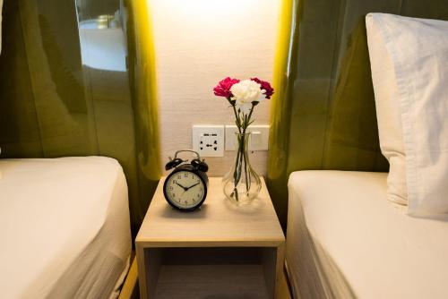 a vase of flowers and an alarm clock on a table between two beds at V Varee Bangkok in Bangkok
