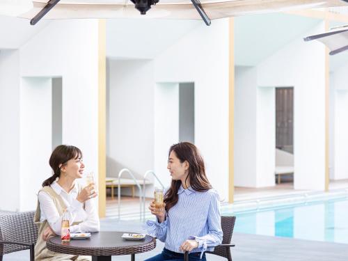 two women sitting at a table with drinks in front of a pool at Garden Terrace Saga Hotel & Resorts in Saga