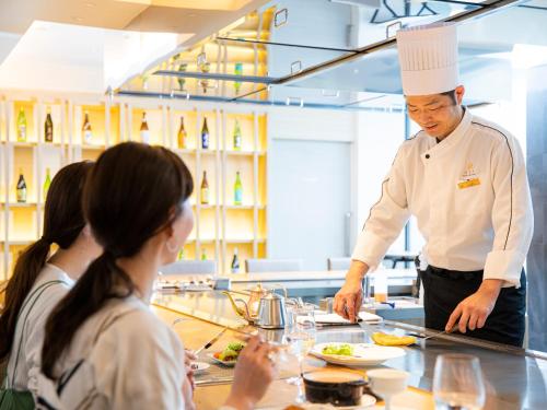a chef preparing food in a kitchen with a group of people at Garden Terrace Saga Hotel & Resorts in Saga
