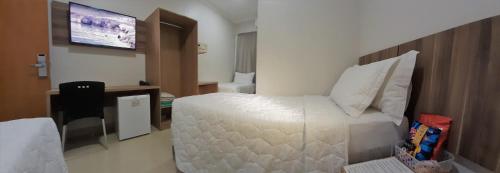a bedroom with a large white bed and a flat screen tv at Hotel Horto in Rondonópolis