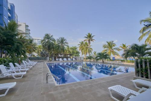 una piscina con sillas blancas y palmeras en Hermoso Apartamento Frente al Mar 2 Habitaciones PAZ146, en Coveñas