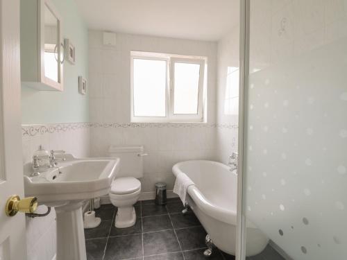 a white bathroom with a tub and a toilet and a sink at Arbour Retreat in Filey