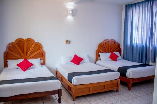 3 camas en una habitación con almohadas rojas. en Hotel Adelita en Zihuatanejo