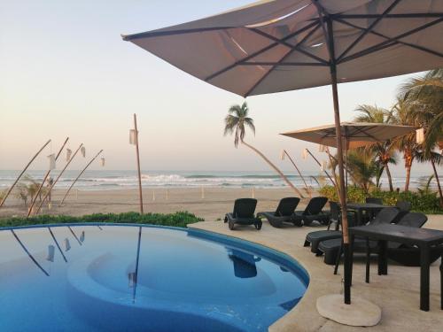 a swimming pool with chairs and an umbrella and the beach at Mishol Bodas Hotel & Beach Club Acapulco Diamante in Acapulco