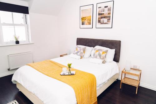 a white bedroom with a bed with a yellow blanket at Detached Coach House in Colchester