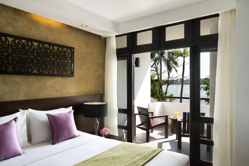 a bedroom with a bed with purple pillows and a balcony at Avani Kalutara Resort in Kalutara
