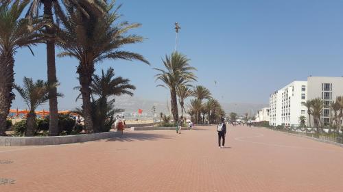 a man in a suit walking down a street with palm trees at Appartment Avenue Hassan II in Agadir