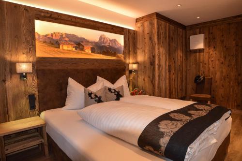 a bedroom with a bed with a painting on the wall at Aurela Mountain Chalets in Selva di Val Gardena