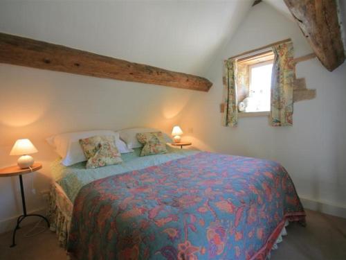 a bedroom with a bed with a blue comforter and a window at Mayfly Cottage in Quenington