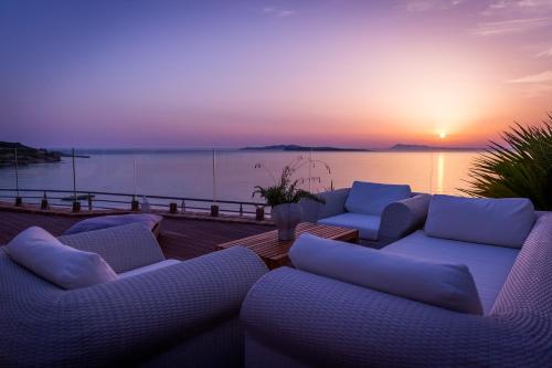 a deck with couches and a sunset on the water at Pictures Suites in Agios Stefanos