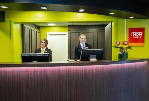 two people sitting at a reception counter in a hotel room at Thon Hotel Slottsparken in Oslo