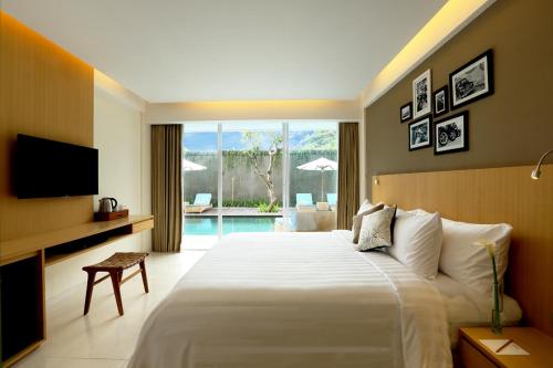 a bedroom with a bed and a television and a pool at Ossotel Legian in Legian